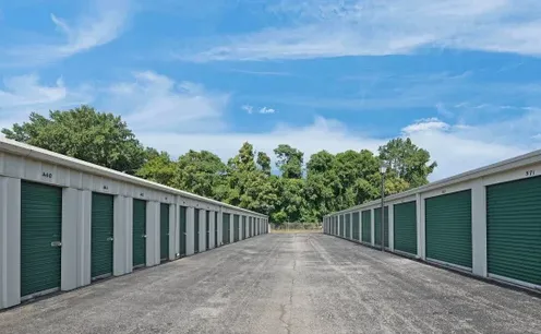 A wide paved drive aisle running between two facing rows of green drive-up storage doors.