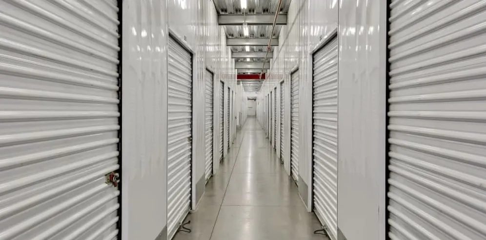 A clean, brightly lit interior corridor lined with white climate-controlled storage doors.